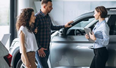 Young couple talking to a sales person in a car showroom, representing the Volkswagen and Audi data breach settlement.