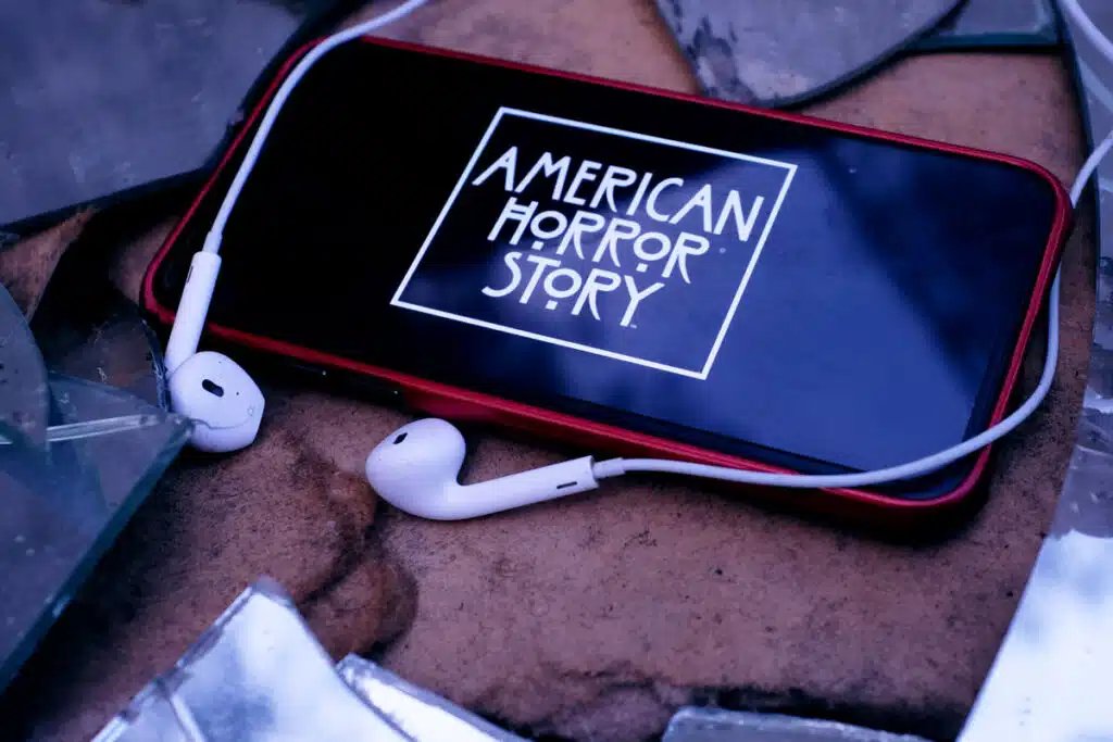 Headphones and Iphone 11 pro with the American Horror Story logo.