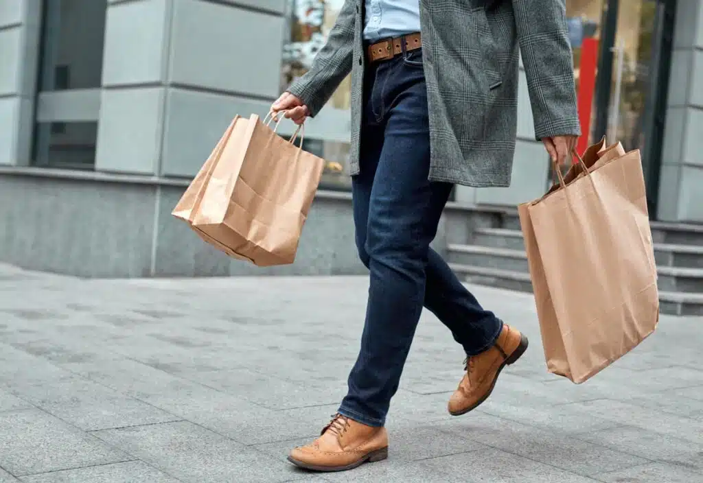 Cropped view of confident adult man in denim casual wear holding shopping paper bags in hands.