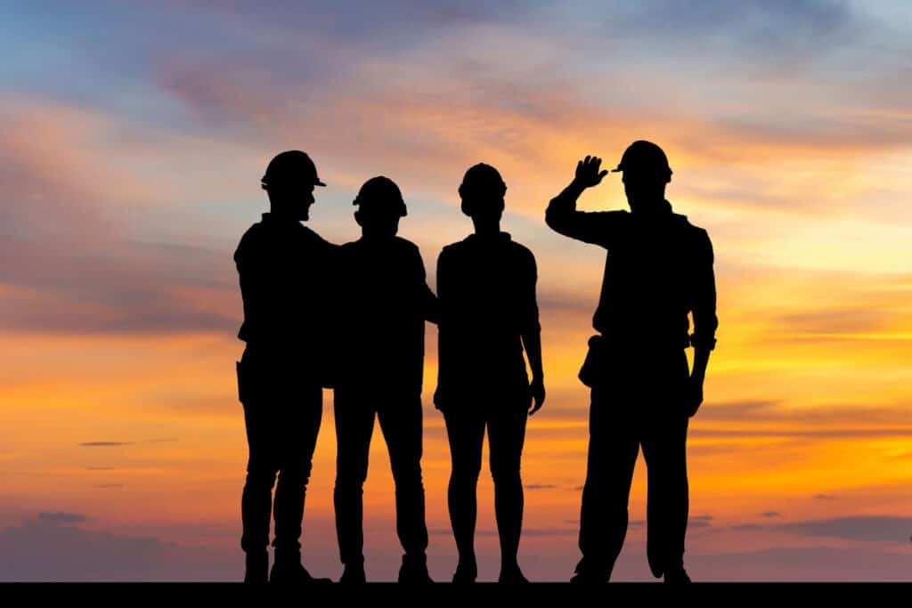 Sihloutte of construction workers against a sunset sky.