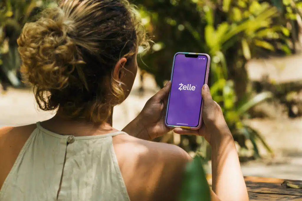 Girl in the park holding a smartphone with Zelle app on the screen.