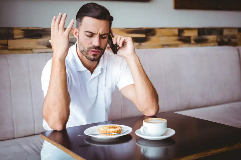 Young man angry on the phone at the cafe, representing the Great Lakes Educational Loan Services settlement.