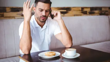 Young man angry on the phone at the cafe, representing the Great Lakes Educational Loan Services settlement.