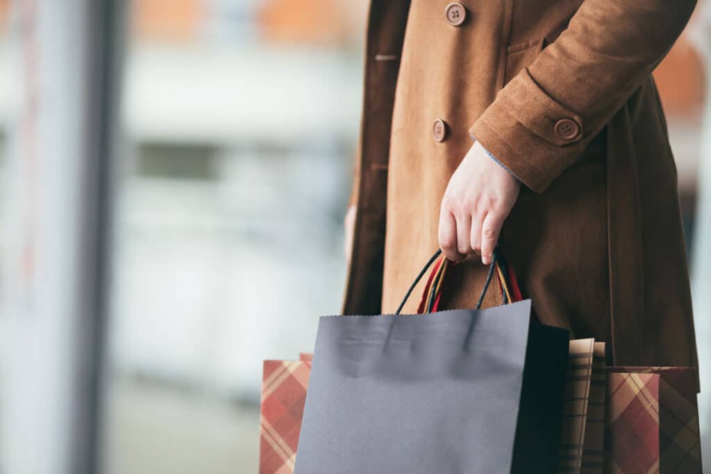 Elegant and modern woman in brown leather jacket or topcoat standing on the city street and holding bunch of shopping bags.