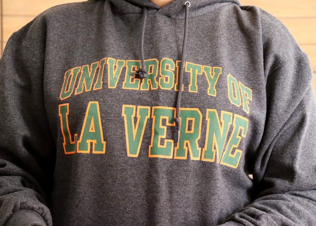 A person wears a grey University of La Verne hoodie with green-and-yellow lettering, representing the tuition settlement.