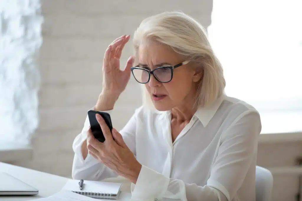 An irritated elderly woman looks at her smartphone after recieving a call.