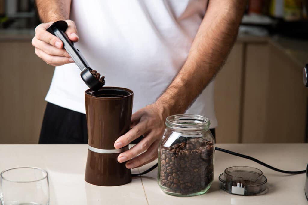 Close up of a man putting coffee beans in a grinder, representing the Kona coffee class action involving Walmart and other retailers.
