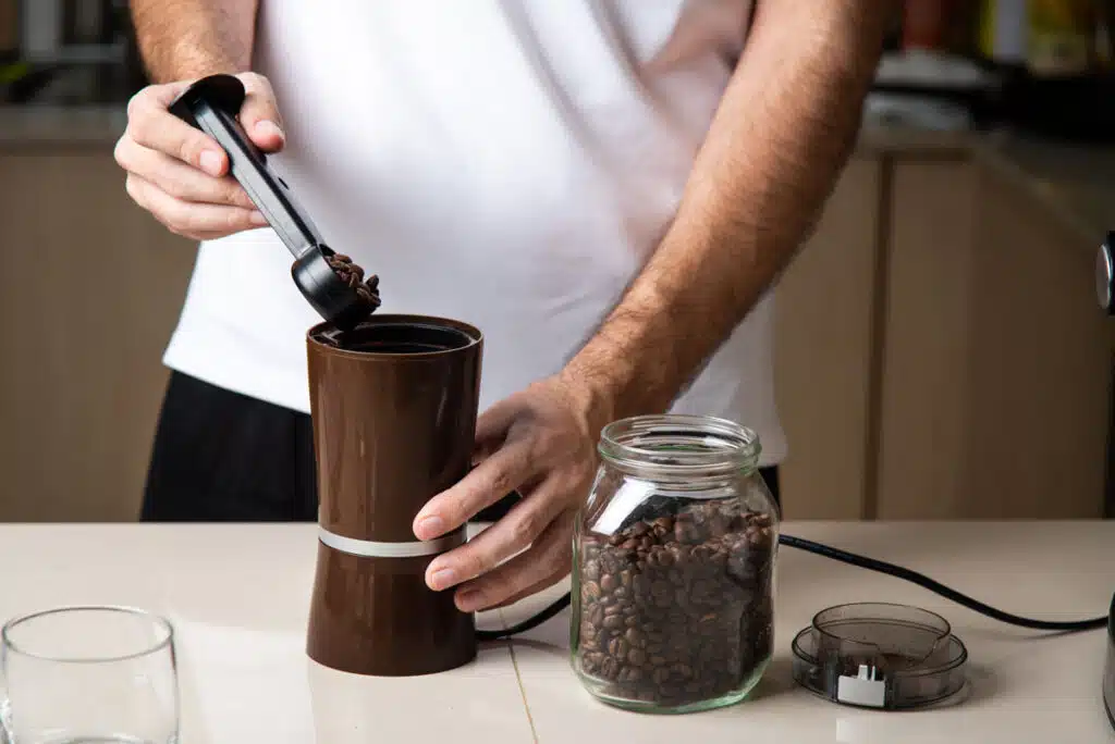 Close up of a man putting coffee beans in a grinder, representing the Kona coffee class action involving Walmart and other retailers.