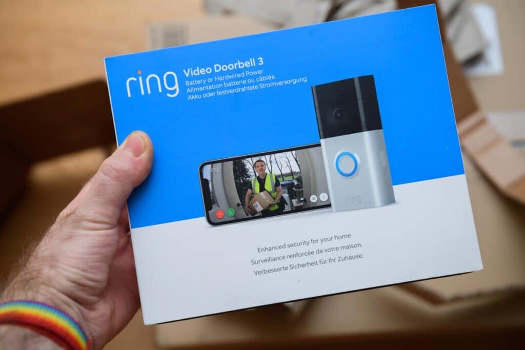 POV male hand holding before unboxing recent parcel with package of new latest Amazon Ring Video Doorbell 3, representing a Ring class action lawsuit.
