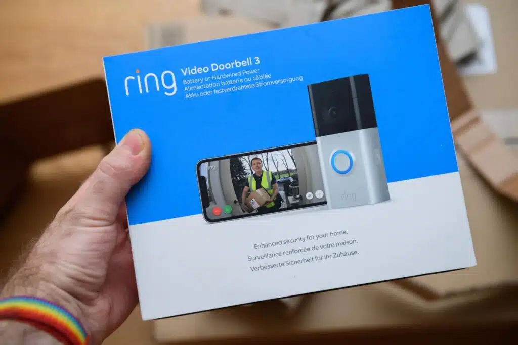 POV male hand holding before unboxing recent parcel with package of new latest Amazon Ring Video Doorbell 3, representing a Ring class action lawsuit.