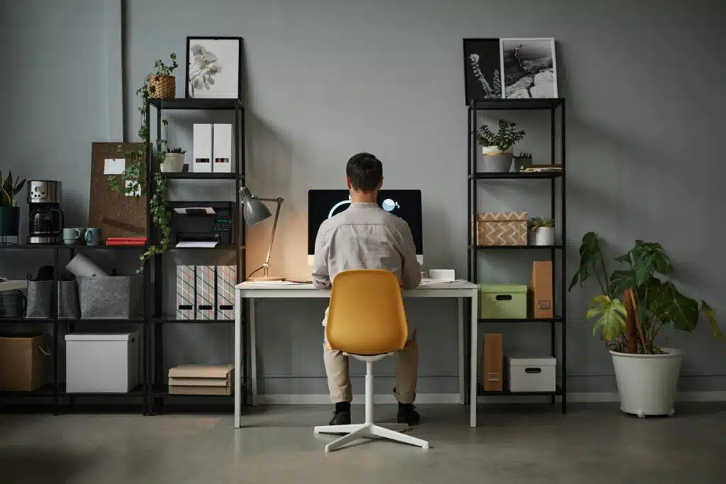 Wide angle back view at man using computer at home office with modern tech interior.