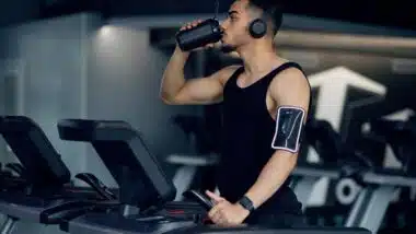 Muscular Arab Guy Drinking Protein Cocktail From Sport Shaker While Training On Treadmill At Gym.