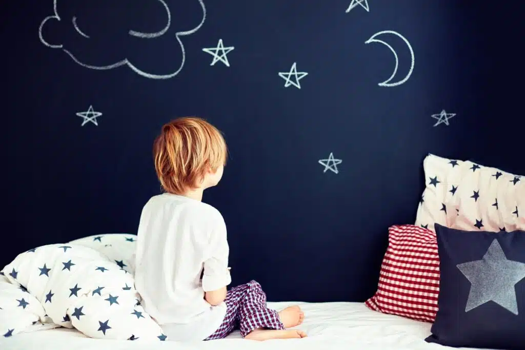 Back view of a young boy in pajamas looking at chalk drawings on his wall, representing the children's pajama and robe recall.