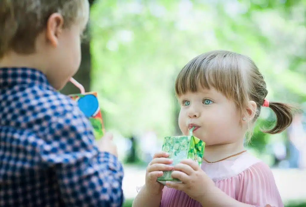 A young girl and a young boy drinking out of juice boxes.