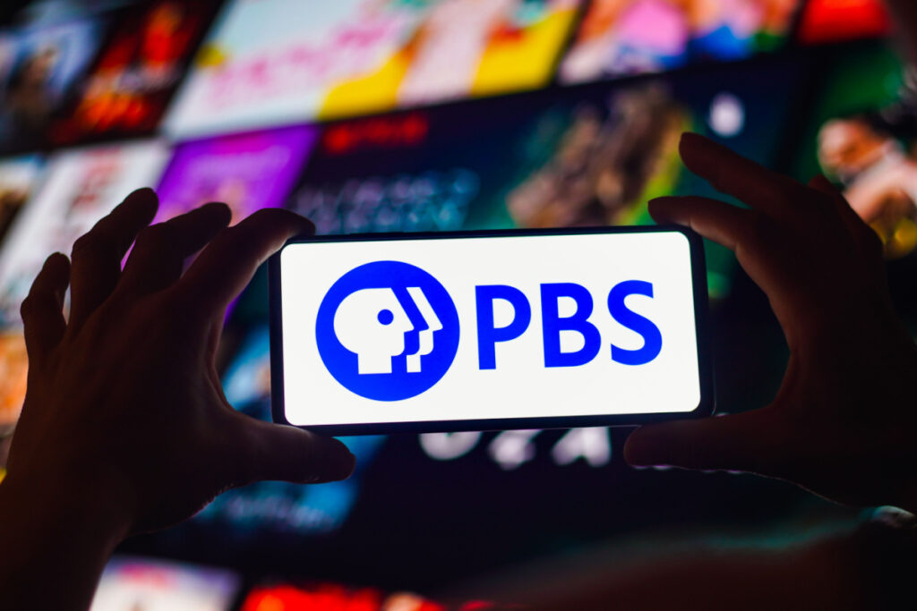 A person holding up a cell phone with PBS logo on the screen.