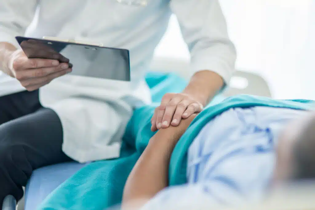 A doctor sitting on bed with a patient while she holds her stomach