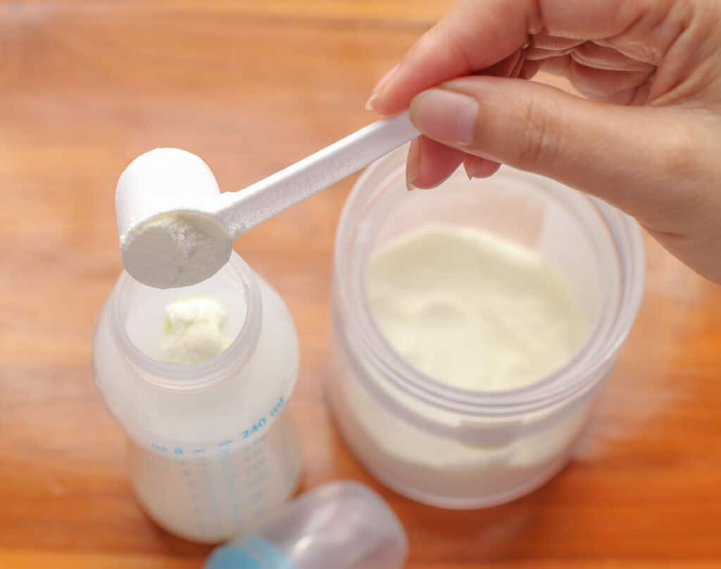 A person preparing a bottle with a scope of formula