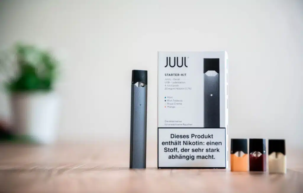 Juul vaping device with cartridges on desk, representing the Juul false advertising class action lawsuit settlement. No receipt or proof of purchase is required for consumers to submit a claim in the Juul class action lawsuit settlement.
