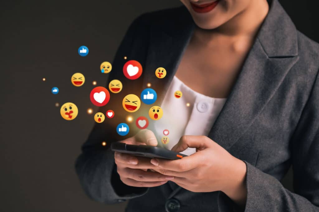 A woman types on a cellphone with emoji flying out of the screen, representing legal emoji