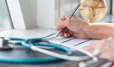 Doctor writing on paper near a stethoscope representing the Orlando Family Physicians class action settlement.