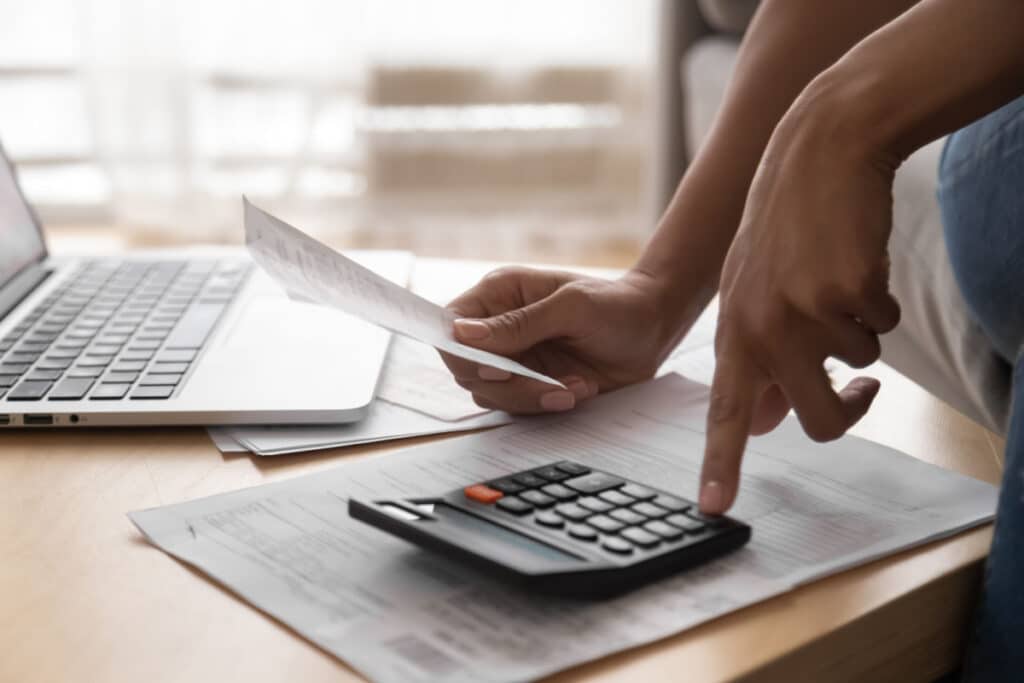 A person using a calculator holding papers representing the PHH mortgage fee settlement.