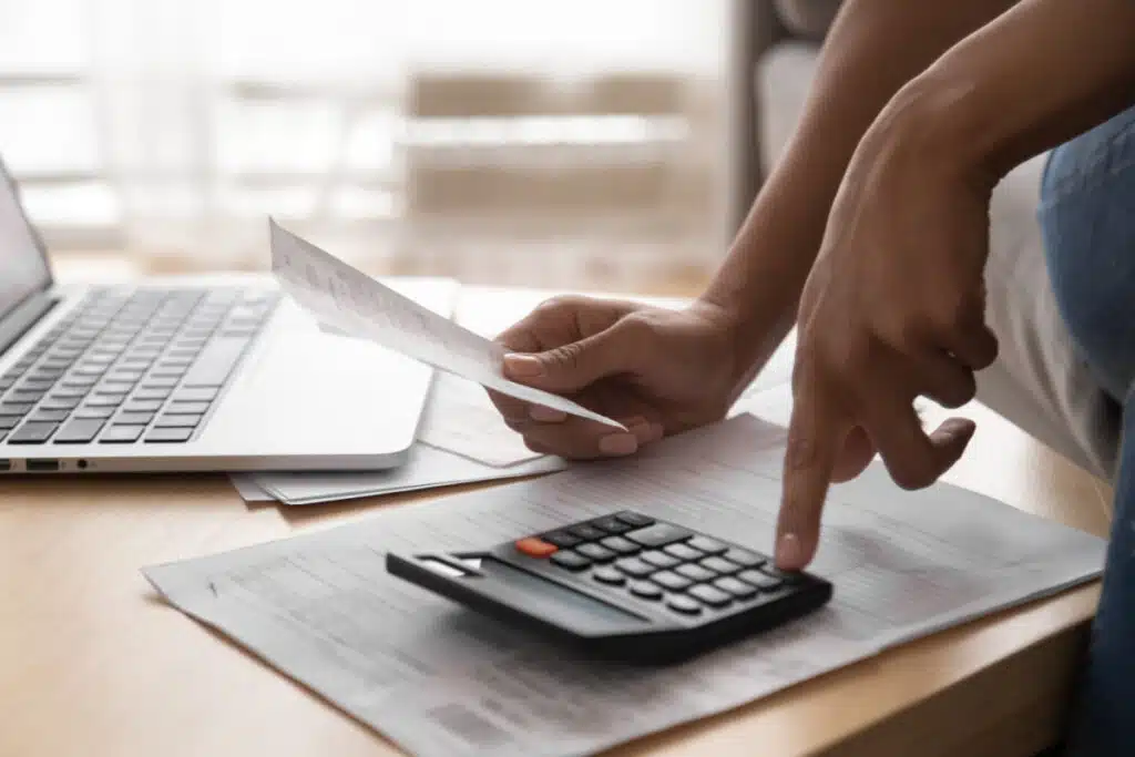 A person using a calculator holding papers representing the PHH mortgage fee settlement.