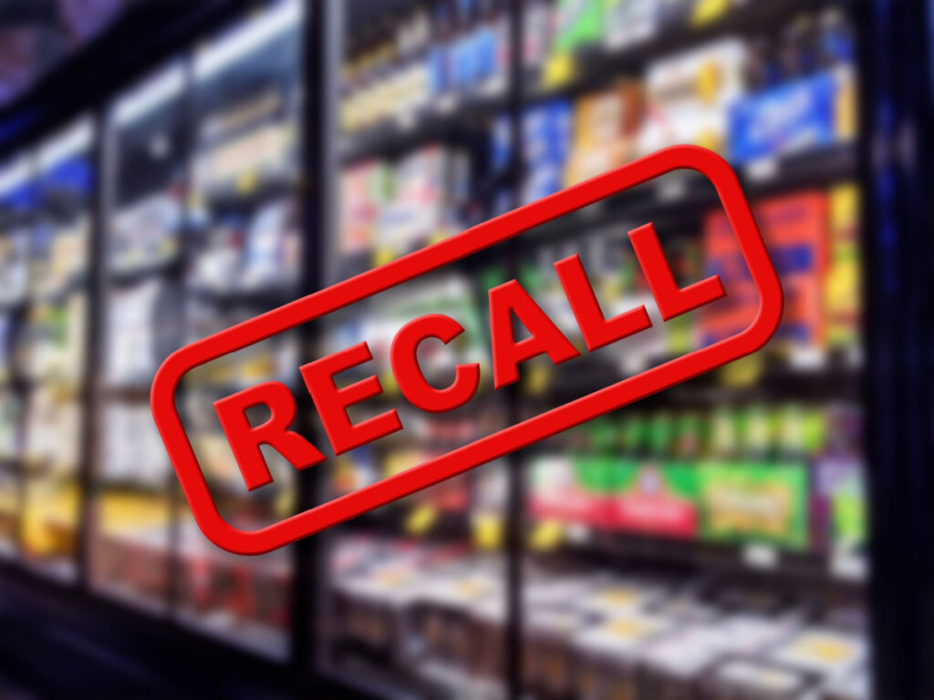 Recall written in red letter over a blurred photo of the frozen section in grocery store