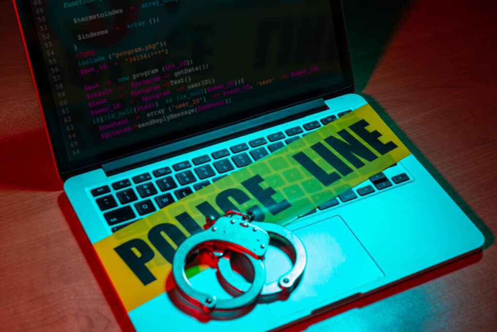 A laptop is seen with yellow police tape and handcuffs on the keyboard, representing the Genesis Market forum FBI seizure