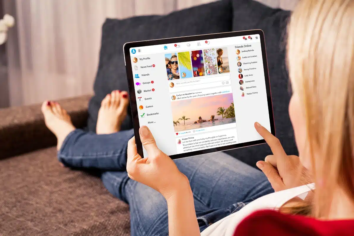 A woman sits with her legs outstretched as she uses a tablet to look at social media, representing the Facebook class action settlement.