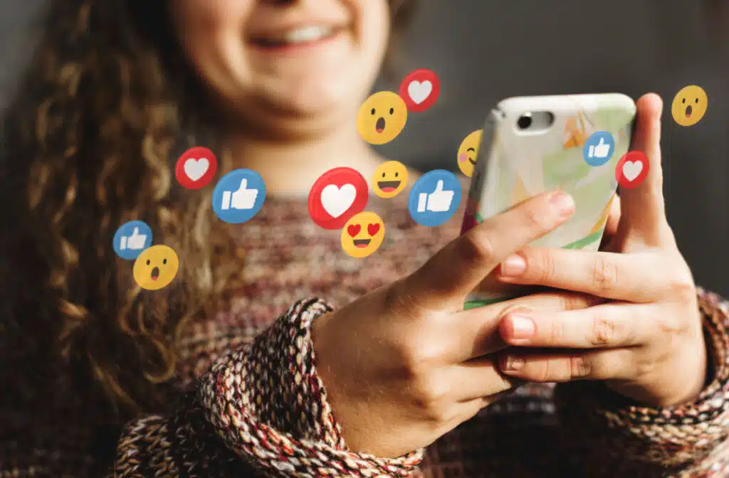 A young girl on her cell phone with emojis surrounding the phone.