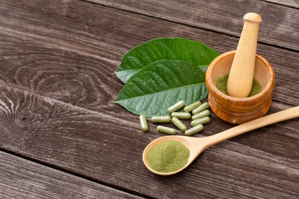Kratom pills next to a pistol and mortar with kratom inside