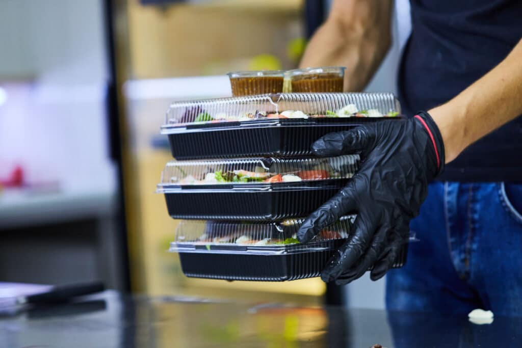 Food service worker holding 3 salads in to-go boxes