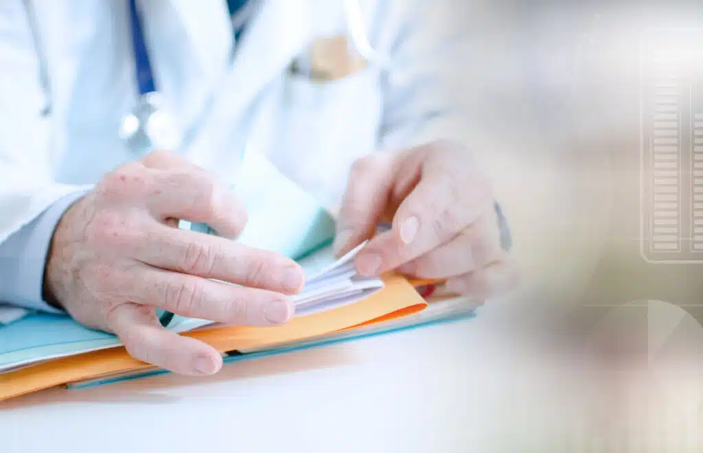 Close up of a doctor looking through a file in a stack of paper on his desk, representing the Medical Review Institute of America (MRIA) data breach class action lawsuit settlement.