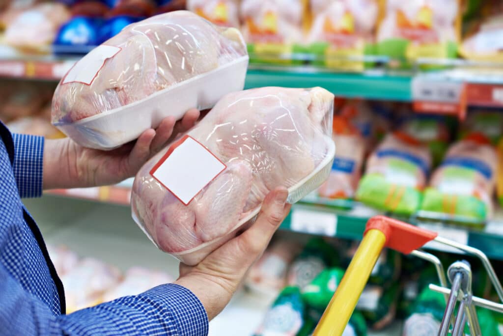 A shopper in a grocery store compares chicken meat, representing the poultry price-fixing settlement