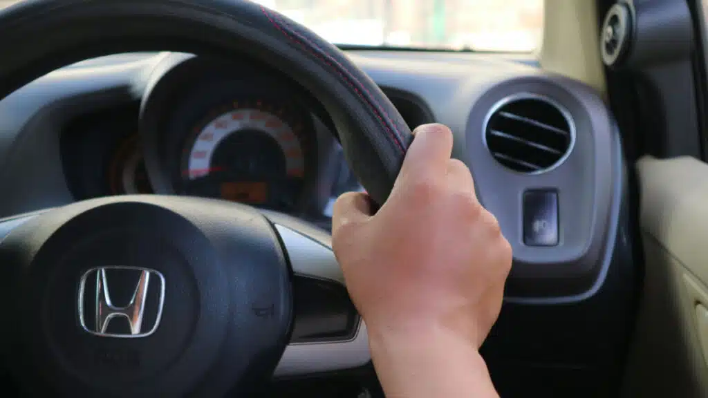 One hand holding on Honda steering wheel.