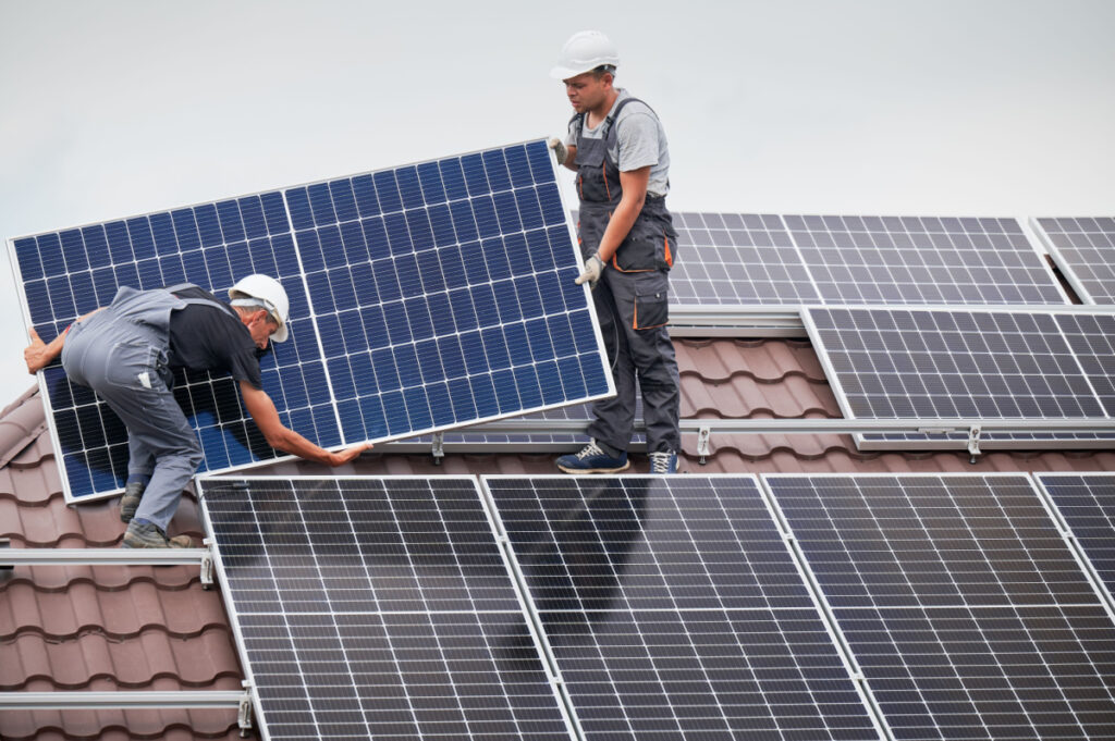 Men technicians carrying photovoltaic solar moduls on roof of house.