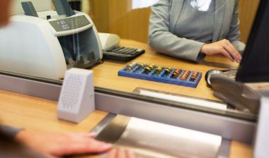 people, money, saving and finance concept - clerk counting coins for customer at bank office or currency exchanger
