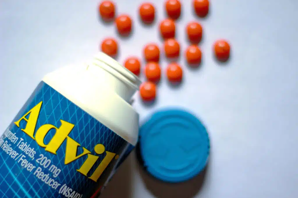 Bottles of advil and pills spread on a white table.