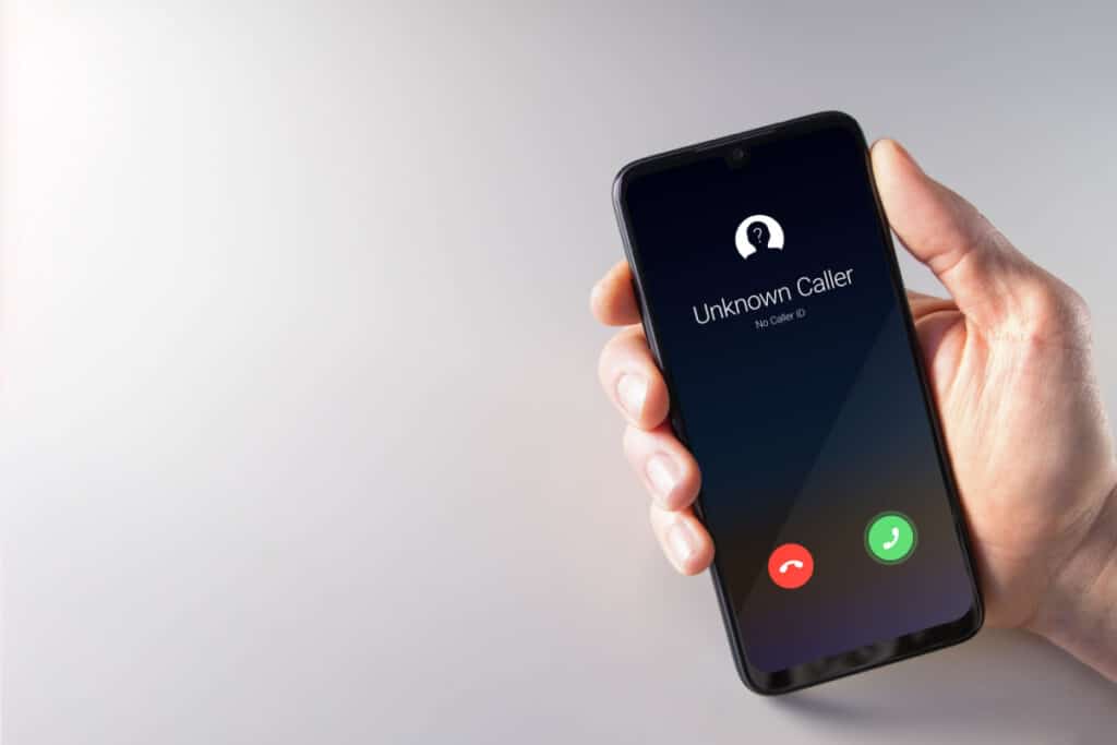 A hand holds a smartphone with unknown caller displayed on screen, representing the telemarketing class action.