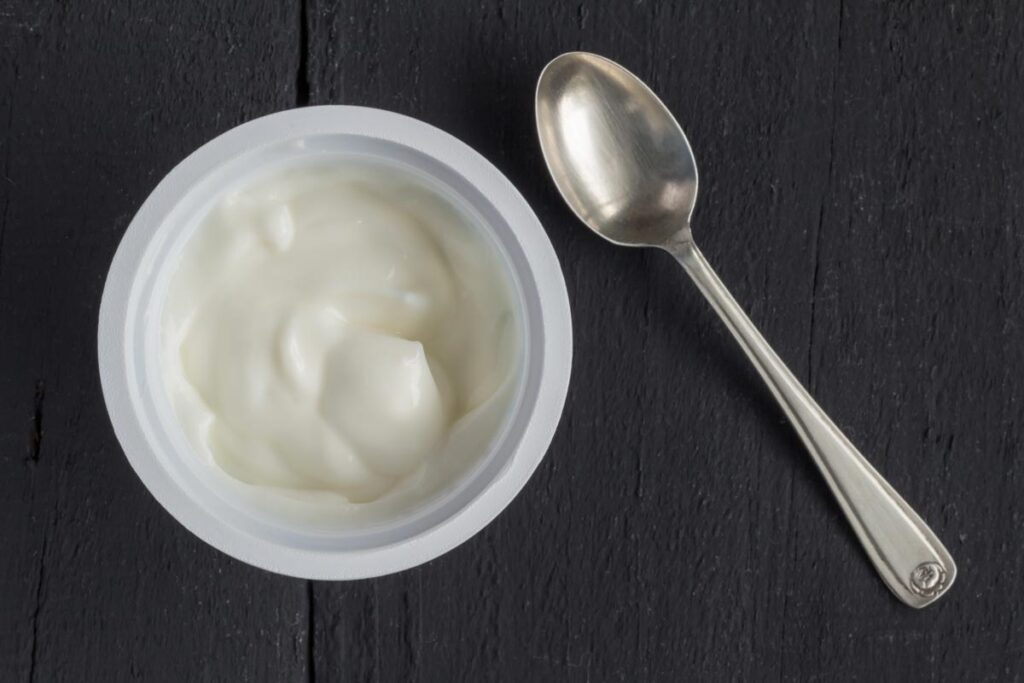 Yogurt in plastic cup on rustic black table with small silver spoon, representing the Costco Ellenos yogurt recall.