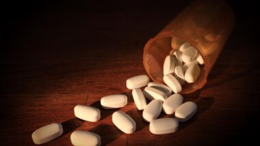 White pills scattered around a pill bottle on a tabletop, representing the Amgen-Horizon merger.