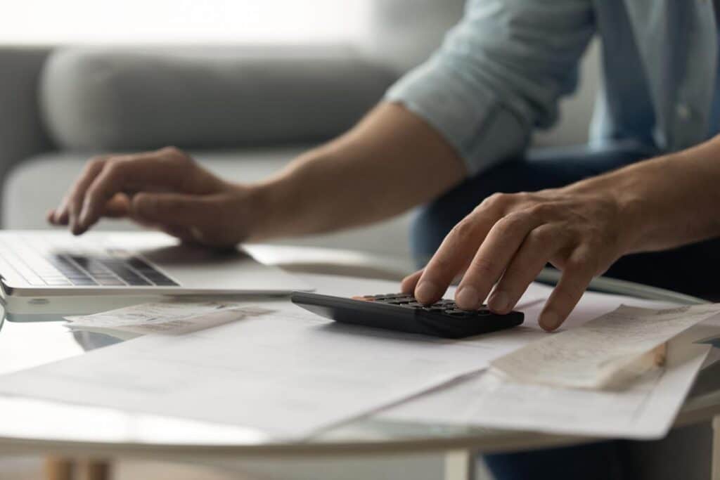Close up of a young male using a laptop calculator to file taxes, representing the IRS free direct tax filing system.