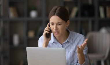 Irritated woman talking on the phone while looking at her laptop, representing the Health Insurance Associates settlement.