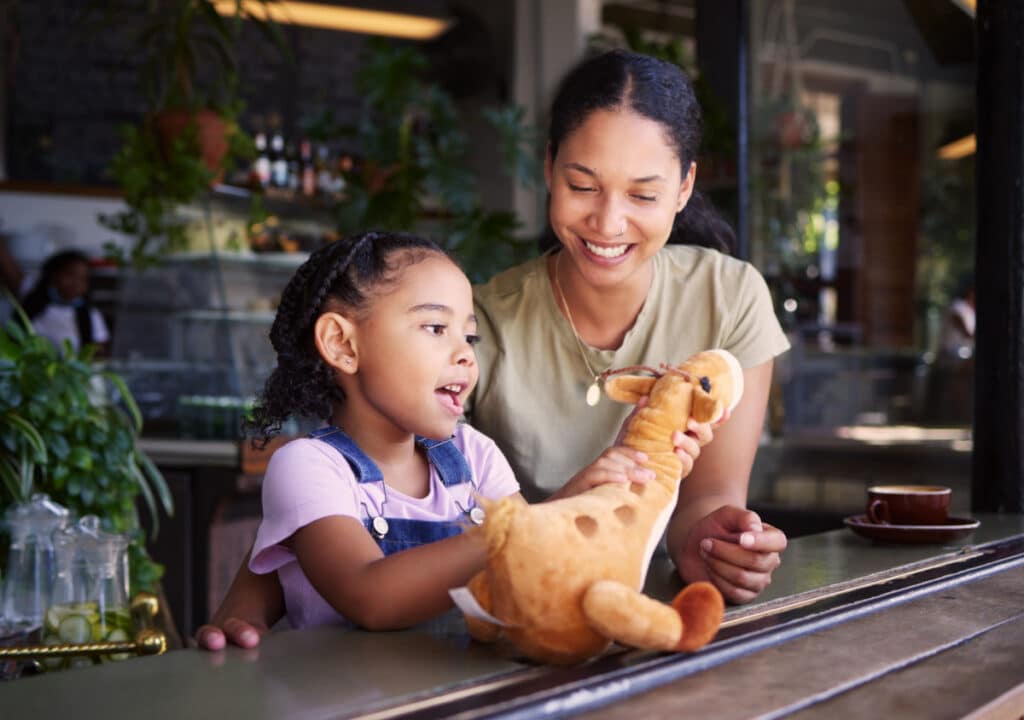 Black family, coffee shop or stuffed animal with a mother and daughter sitting in the window of a restaurant together.