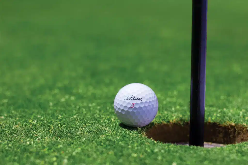 Close up of a golf ball next to a hole, representing the PGA/LIV merger.