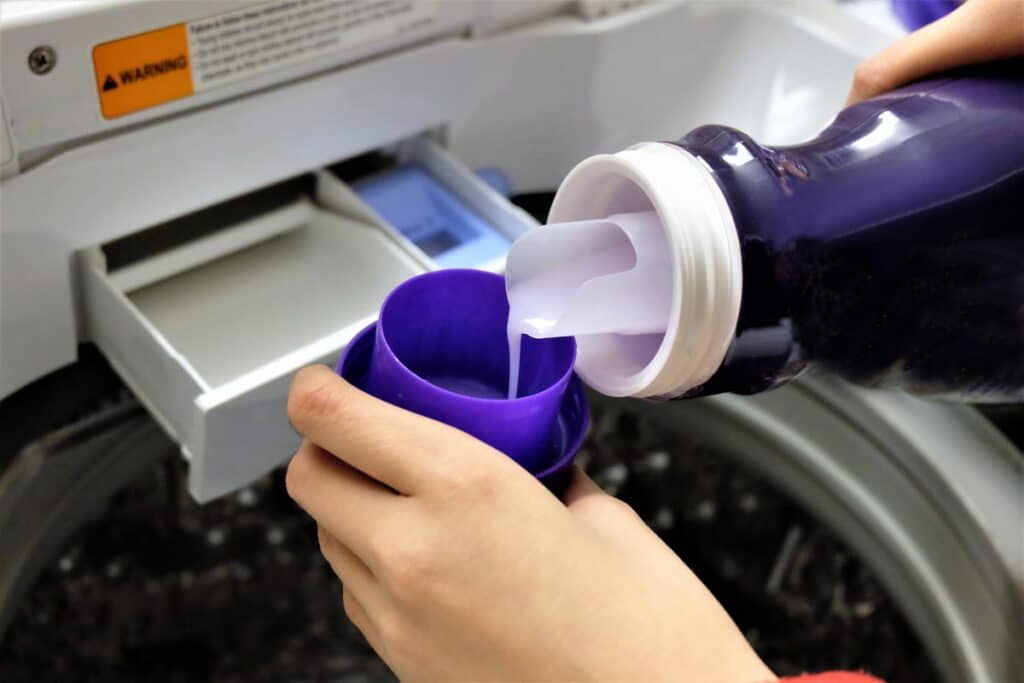 Close up of hand pouring laundry detergent into cup, representing the Woolite class action lawsuit.