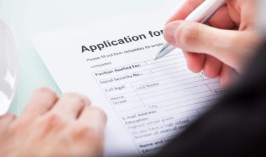 Close up of a males hands filling out a job application, representing the Kaiser Foundation Hospitals settlement.
