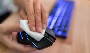Close up of a hand cleaning a computer mouse with a wipe.