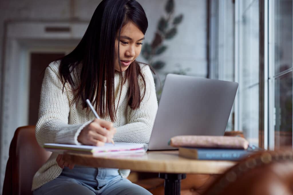 A female student studying with her laptop in a coffee shop, representing the Marymount Manhattan College data breach class action lawsuit settlement.