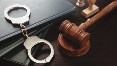 A judges gavel and handcuffs on a law book, representing the COVID relief funds scam charges.